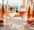 Two rosé wine glasses on a sunlit table beside bottles, with strawberries, cheese, and crackers; labels read Dry Rosé and Sweet Rosé.