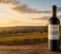 Bottle of Pertaringa Yeoman red wine on a weathered wooden table with a vineyard at sunset in the background.
