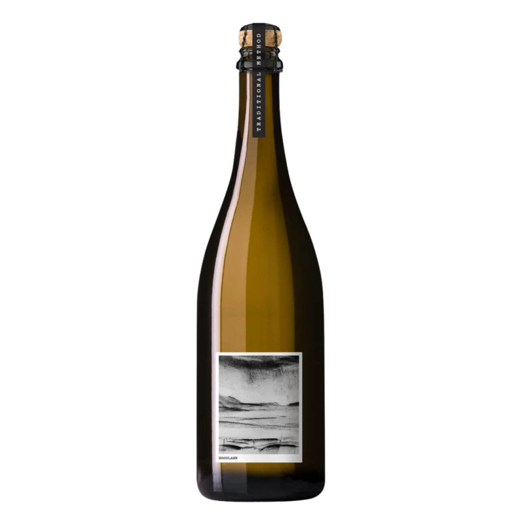 Brown champagne bottle with cork and wire cage, label shows a black-and-white landscape image on the front panel.